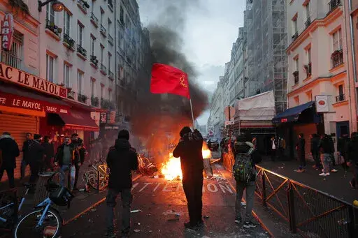 A members of Kurdish community waves the Kurdish communist flags next to a barricade on fire at the crime scene where a shooting took place in Paris, Friday, Dec. 23, 2022. Skirmishes erupted in the neighbourhood a few hours after the shooting, as members of the Kurdish community shouted slogans against the Turkish government, and police fired tear gas to disperse an increasingly agitated crowd. A shooting targeting a Kurdish cultural center in Paris Friday left three people dead and three other