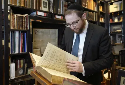 Rabbi Nicky Liss looks through items in a collection belonging to Professor David Latchman of memorabilia related to the history of British Jews, in London, Friday, April 28, 2023. Rabbi Nicky Liss won’t be watching King Charles III’s coronation. He’ll be doing something more important praying for the monarch on the Jewish sabbath. On Saturday, he will join rabbis across Britain in reading a prayer in English and Hebrew that gives thanks for the new king in the name of the “one God who c