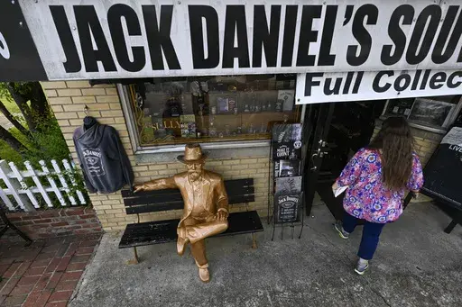 A statue of Jack Daniels sits on a bench as a visitor enters a souvenir shop in the town where the distillery is located Wednesday, June 14, 2023, in Lynchburg, Tenn. A destructive and unsightly black fungus which feeds on ethanol emitted by whiskey barrels has been found growing on property near the distillery's nearby barrelhouses which has resulted in a lawsuit against it. (AP Photo/John Amis)