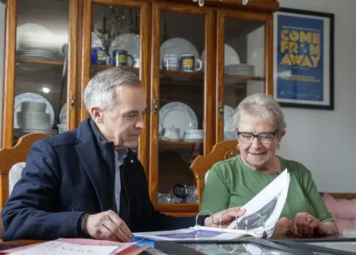 Canada Prime Minister Mark Carney looks through a photo album with Beulah Cooper at her home in Gander, Newfoundland, Monday, March 24, 2025. (Frank Gunn/The Canadian Press via AP)