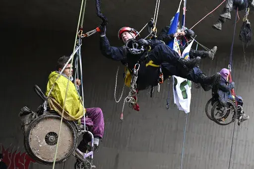 A police height rescuer helps an environmental activist in a wheelchair to the ground near the city of Sitz, Germany, Jan. 16, 2023. Climate activists in wheelchairs rappelled down from a highway bridge on the A44 on Monday morning to protest against the destruction of the nearby village Luetzerath for the expansion of a lignite coal mine. The bridge is about four kilometers from the town of Luetzerath. (Roberto Pfeil/dpa via AP)