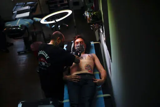 A man, wearing a protective face mask to prevent the spread of coronavirus, is tattooed at Paul and Friends tattoo parlour in downtown Brussels, March 26, 2021. The European Union is imposing restrictions on the inks that tattoo artists can use as of Wednesday, Jan. 5, 2022. The EU says it is a necessary move to protect the health of consumers because thousands of chemical elements now in use can cause anything from allergic reactions to cancer. The tattoo industry complains it is unfairly targe