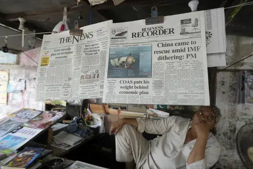 A vendor sits beside a copy of a morning newspaper which reports missing Titanic submersible and onboard five people, including Pakistani nationals Shahzada Dawood and his son Suleman, at a stall, in Karachi, Pakistan on June 21, 2023. The saga of a lost submersible that had gone into the depths of the ocean to see the Titanic wreckage rippled across the national and global conversation. But a far bigger disaster days earlier, the wrecking of a ship off Greece filled with migrants, didn't become