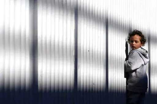 A young migrant stands by a fence at an entry point for asylum seekers Wednesday, Dec. 21, 2022, in Tijuana, Mexico. Thousands of migrants gathered along the Mexican side of the southern border Wednesday, camping outside or packing into shelters as they waited for the U.S. Supreme Court to decide whether and when to lift pandemic-era restrictions that have prevented many from seeking asylum. (AP Photo/Marcio Jose Sanchez)
