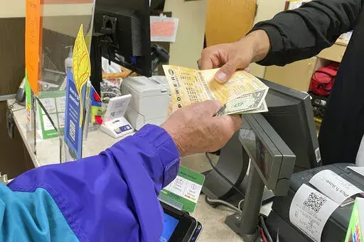 From behind the lottery counter at a Pick 'n Save store in Madison, Wis., Djuan Davis hands Powerball tickets to Arpad Jakab, a retired utility worker who said it's his first time buying them. The Powerball jackpot recently reached a record high of $1.6 billion. (AP Photo/Harm Venhuizen)