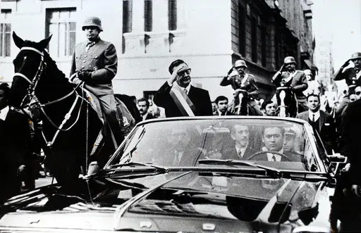 Chilean President Salvador Allende salutes from an open vehicle as General Augusto Pinochet rides on horseback at left in Santiago, Chile, May 21, 1972. (AP Photo/File)
