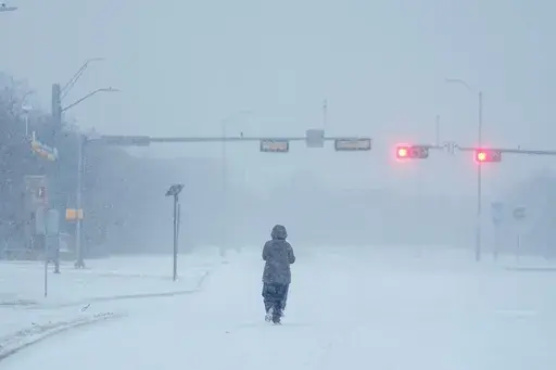 A jogger trots on a snow-covered road during a winter storm, Jan. 15, 2024, in Grand Prairie, Texas. Winter weather brings various hazards that people have to contend with to keep warm and safe. These dangers can include carbon monoxide poisoning, hypothermia and frozen pipes that can burst and make homes unlivable. Public safety officials and experts say there are multiple ways people can prepare themselves to avoid these hazards and keep themselves safe. (AP Photo/Julio Cortez, file)