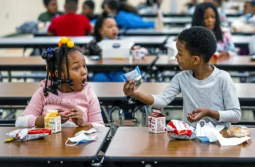 First graders, from left, Kendal Kates and Ryan Kenney are excited about the contents of their boxed lunches at Langley K-8 School, Dec. 23, 2021, in the Sheraden neighborhood in Pittsburgh. The Biden administration has issued transitional standards for school lunches that are meant to get cafeterias back on a healthier course as they recover from pandemic and supply chain disruptions.  The “bridge” rule announced by the U.S. Agriculture Department on Friday extends emergency flexibilities f