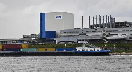 A container ship passes the Ford car plant in Cologne, Germany, May 4, 2020. Ford said that it will cut 3,800 jobs in Europe over the next three years in an effort to streamline its operations as it contends with economic headwinds and increasing competition on electric cars. The automaker said that 2,300 jobs will go in Germany. (AP Photo/Martin Meissner, File)