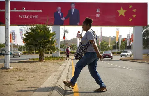 A woman crosses the street near a billboard commemorating the state visit of Chinese President Xi Jinping in Port Moresby, Papua New Guinea, Nov. 15, 2018. China wants 10 small Pacific nations to endorse a sweeping agreement covering everything from security to fisheries in what one leader warns is a “game-changing” bid by Beijing to wrest control of the region. (AP Photo/Mark Schiefelbein, File)