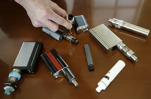 In this April 10, 2018 file photo, a high school principal displays vaping devices that were confiscated from students in such places as restrooms or hallways at the school in Massachusetts. Schools around the country are installing sensors and cameras to crack down on student vaping, and handing out harsh punishments for many who are caught. Schools have invested millions of dollars in the surveillance technology, including federal COVID-19 emergency relief money meant to help schools through t