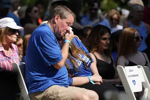 A visitor wipes tears at a remembrance ceremony in Highland Park, Ill., Tuesday, July 4, 2023. One year after a shooter took seven lives at the city's annual parade, community members are planning to honor the victims and reclaim the space to move forward. (AP Photo/Nam Y. Huh)