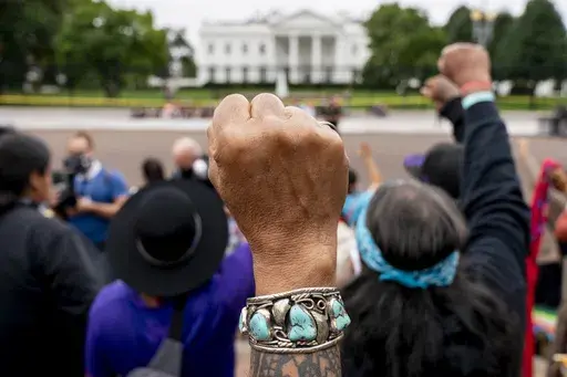 Wolf Ramerez of Houston, Texas, center, joins others with the Carrizo Comecrudo Tribe of Texas in holding up his fists as indigenous and environmental activists protest in front of the White House in Washington, Oct. 11, 2021. Members of the Native American Journalists Association are voting on whether to change the name to the Indigenous Journalists Association. (AP Photo/Andrew Harnik, file)