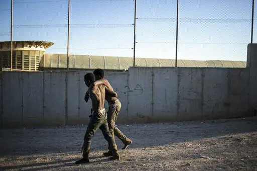 A migrant helps another as they arrive on Spanish soil after crossing the fences separating the Spanish enclave of Melilla from Morocco, in Melilla, Spain, Thursday March 3, 2022. Hundreds of Africans have tried to climb over the fences separating the Spanish city of Melilla from Morocco for the second consecutive day and the Spanish government's delegation in Melilla says that 380 of 1,200 migrants who had attempted to cross managed to overcome the double 6-meter (20-feet) barrier that perimete