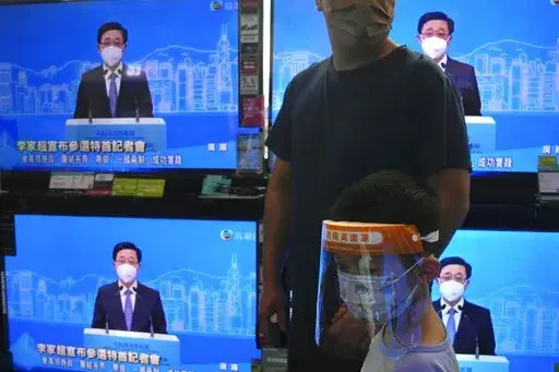 The TV screens show former Hong Kong Chief Secretary John Lee speaks during an online press conference to announce his candidacy for the Election of the Hong Kong chief executive, in Hong Kong, Saturday, April 9, 2022. (AP Photo/Kin Cheung)