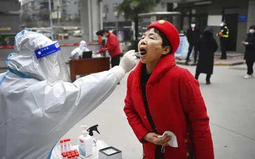 In this photo released by China's Xinhua News Agency, a worker wearing protective gear gives a COVID-19 test to a woman at a testing site in Xi'an in northwestern China's Shaanxi Province, Tuesday, Jan. 4, 2022. China is reporting a major drop in local COVID-19 infections in the northern city of Xi'an, which has been under a tight lockdown for the past two weeks. (Tao Ming/Xinhua via AP)