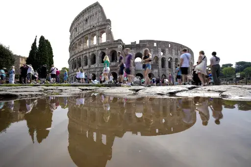 Tourists walk by the ancient Roman Colosseum as it's reflected in a puddle, in Rome, Sept. 5, 2024. (AP Photo/Andrew Medichini, file)