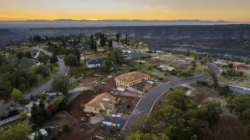 The sun sets over Valley Ridge Drive, Thursday, Oct. 26, 2023, in Paradise, Calif. Empty lots, homes under construction and residences built after the Camp Fire line the street. (AP Photo/Noah Berger)