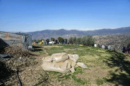 Bags of harvested cannabis left to dry in the sun as mourners gather around a hill at the funeral of five year old Rayan after his body was retrieved from a deep well, in the village of Ighran in Morocco's Chefchaouen province, Monday, Feb. 7, 2022. The death of a 5-year-old boy trapped for days in the dark depths of a well symbolizes for many villagers a curse that haunts their remote mountainous region in northern Morocco. Rif is dirt poor, neglected and dependent on its illegal cannabis crop 