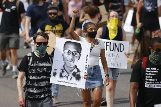 Demonstrators carry placards as they walk down Sable Boulevard during a rally and march over the death of Elijah McClain in Aurora, Colo., on June 27, 2020. A group of police officers and paramedics charged in the death of McClain, a 23-year-old Black man who was forcibly restrained and injected with a powerful sedative, are scheduled to appear in court Friday, Jan. 20, 2023, to enter pleas to the allegations. (AP Photo/David Zalubowski, File)