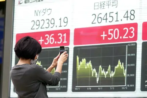 A person takes photos of an electronic stock board showing Japan's Nikkei and New York Dow indexes at a securities firm Wednesday, Oct. 12, 2022, in Tokyo. Asian shares were mostly lower on Wednesday following another volatile day on Wall Street, as traders braced for updates on inflation and corporate earnings. (AP Photo/Eugene Hoshiko)