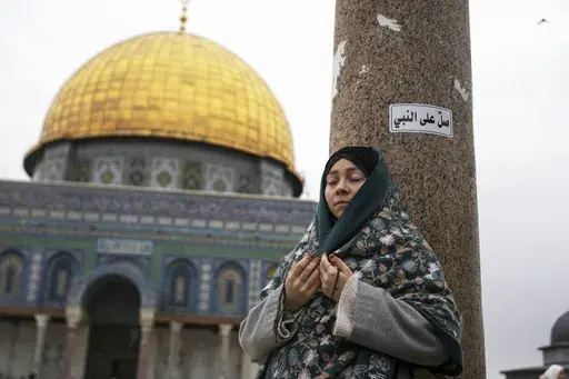 A woman prays at the Al-Aqsa Mosque compound during the first Friday Prayers of the Muslim holy month of Ramadan in the Old City of Jerusalem, Friday, March 7, 2025. Arabic on top right reads: "Pray for the Prophet." (AP Photo/Mahmoud Illean)