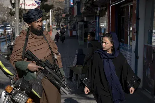 A Taliban fighter stands guard as a woman walks past in Kabul, Afghanistan, on Dec. 26, 2022. The United Nations' human rights chief on Tuesday Dec. 27, 2022. A U.N. report on Monday, May 8, 2023 condemned the Taliban for their harsh rule since seizing power in Afghanistan — including public execution, lashings, and amputations — and for ignoring international calls to respect human rights and freedoms. (AP Photo/Ebrahim Noroozi, File)