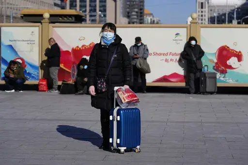 A traveler waits outside the Beijing railway station with her suitcase in Beijing, China, Friday, Jan. 28, 2022. The Beijing Winter Olympics is coinciding with the Chinese Lunar New Year and renewed Covid outbreaks prompting the Chinese authorities to call on the public to stay where they are instead of traveling to their hometowns for the year's most important family holiday. (AP Photo/Ng Han Guan)