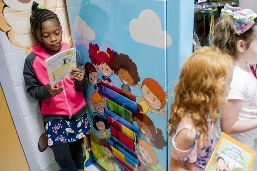 Janaya Sells, 7, reads a token-bought book on Sept. 26, 2019, during a ribbon cutting for an Inchy the Worm book vending machine at R.E. Stevenson Elementary School in Russellville, Ky. For decades, there has been a clash between two schools of thought on how to best teach children to read, with passionate backers on each side of the so-called reading wars. But the approach gaining momentum lately in American classrooms is the so-called science of reading. (Bac Totrong/Daily News via AP, File)