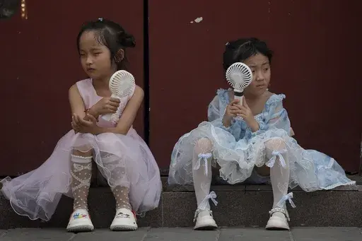 Children cool themselves with electric fans as they take a rest near the Forbidden City on a hot day in Beijing, June 25, 2023. The National Oceanic and Atmospheric Administration said Thursday, July 13, an already warming Earth steamed to its hottest June on record. (AP Photo/Andy Wong, File)