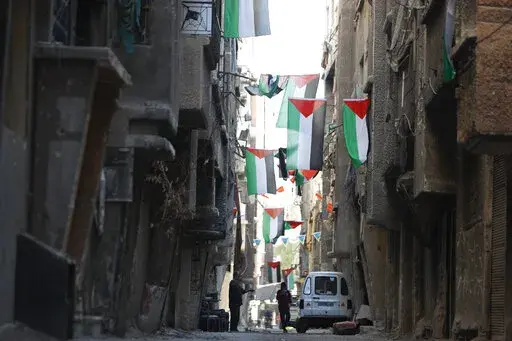 People walk under Palestinian flags in Yarmouk camp in Damascus Syria that has seen heavy fighting during the civil war, Wednesday, Nov. 2, 2022. A trickle of residents has returned to Yarmouk, the large Palestinian refugee camp-turned-Damascus neighborhood that was devastated in the country's civil war. (AP Photo/Omar Sanadiki, File)