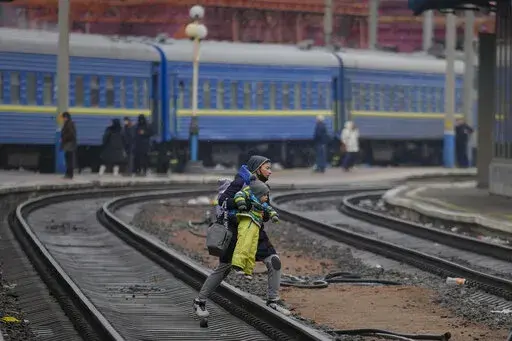 A woman carries a baby over the tracks trying to board a Lviv bound train, in Kyiv, Ukraine, Thursday, March 3, 2022. Ukrainian President Volodymyr Zelenskyy's office says a second round of talks with Russia aimed at stopping the fighting that has sent more than 1 million people fleeing over Ukraine's borders, has begun in neighboring Belarus, but the two sides appeared to have little common ground. (AP Photo/Vadim Ghirda)