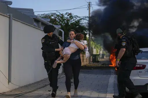 Israeli police officers evacuate a woman and a child from a site hit by a rocket fired from the Gaza Strip, in Ashkelon, southern Israel, Saturday, Oct. 7, 2023. Israel and Hamas have both been accused of breaking the rules of armed conflict. Hamas killed hundreds of civilians and abducted scores more when it attacked southern Israel on Oct. 7. Israel has bombarded Gaza and told more hundreds of thousands of Palestinians to leave their homes. The United Nations says it is collecting evidence of 