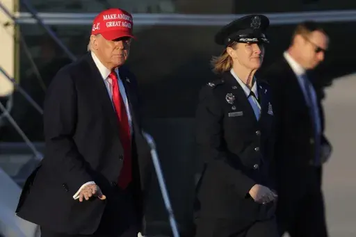 President Donald Trump, left, gestures as is escorted by Air Force Col. Angela Ochoa, commander of the 89th Airlift Wing, center, as he walks from Marine One before boarding Air Force One, Friday, Feb. 28, 2025, at Joint Base Andrews, Md. (AP Photo/Luis M. Alvarez)
