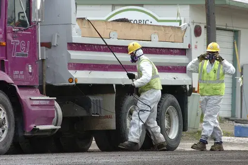 Unidentified road workers wear protective gear against possible asbestos contamination as they load material from a road resurfacing project in downtown Libby, Mont., April 28, 2011. A health clinic in the Montana town that's plagued by deadly asbestos contamination is liable for almost $6 million in penalties and damages after it submitted hundreds of false claims for government benefits. (AP Photo/Matthew Brown, File)