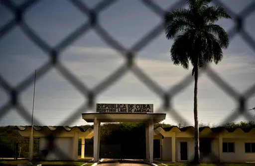 In this photo reviewed by U.S. military officials, a building in Cuba carries the Spanish message "Republic of Cuba. Free American Territory," behind a gate marking the border with the U.S. Guantanamo Bay naval base in Cuba, June 6, 2018. (AP Photo/Ramon Espinosa, File)