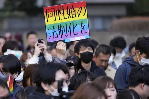 A supporter for the LGBTQ+ community holds up a poster as plaintiffs speak in front of media members by the main entrance of the Tokyo district court after hearing the ruling regarding LGBTQ+ marriage rights, in Tokyo, on March 14, 2024. The poster reads, "Legalize the same-sex marriage." A Japanese high court has approved a legal gender change for a transgender woman without requiring the usual compulsory gender-affirming surgery. The Hiroshima High Court ruled Wednesday July 10, 2024 that the 