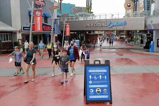 Signs about social distancing and other protocols are seen about the theme park as guests walk by at Universal Orlando Resort Wednesday, June 3, 2020, in Orlando, Fla.   Company officials said Wednesday, Jan. 12, 2022 that workers at Universal’s theme parks must be fully vaccinated by Feb. 9 or be required to take a test every week.   (AP Photo/John Raoux, File)
