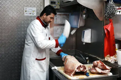 A butcher cuts halal meat in a butcher shop, in Paris, Wednesday, April 13, 2022. Far-right presidential candidate Marine Le Pen is alarming both Muslims and Jews in France with a pledge to ban the ritual slaughter of animals if elected. (AP Photo/Thibault Camus)