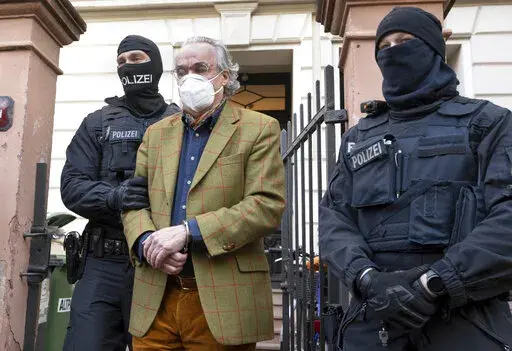 Masked police officers lead Heinrich XIII Prince Reuss, center, to a police vehicle during a raid against so-called 'Reich citizens' in Frankfurt, Germany, Wednesday, Dec. 7, 2022. Thousands of police carried out a series of raids across much of Germany on Wednesday against suspected far-right extremists who allegedly sought to overthrow the state by force. Federal prosecutors said some 3,000 officers conducted searches at 130 sites in 11 of Germany's 16 states against adherents of the so-called