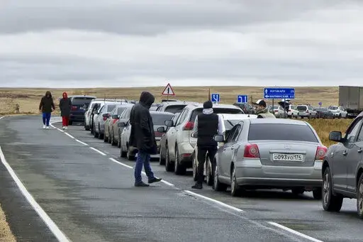 People walk next to their cars queuing to cross the border into Kazakhstan at the Mariinsky border crossing, about 400 kilometers (250 miles) south of Chelyabinsk, Russia, Tuesday, Sept. 27, 2022. Officials say about 98,000 Russians have crossed into Kazakhstan in the week since President Vladimir Putin announced a partial mobilization of reservists to fight in Ukraine. (AP Photo)