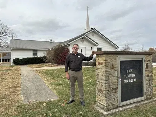 Pastor Kenny Batson stands near a sign displaying the worship service times of Grace Fellowship Church on Nov. 16, 2023, in El Dorado Springs, Mo. Batson was convicted of a series of crimes in the 1990s but became a Christian pastor after being released from prison. He was pardoned by Missouri Gov. Mike Parson. (AP Photo/David A.Lieb)