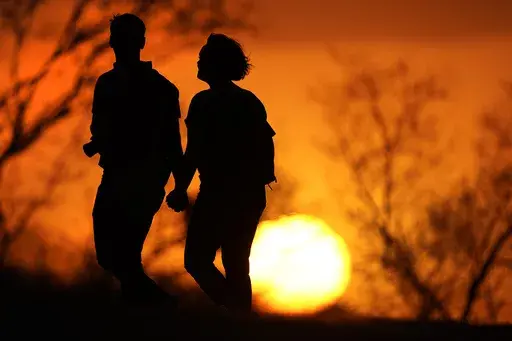 A couple walks through a park at sunset, March 10, 2021, in Kansas City, Mo. U.S. life expectancy rose in 2022 — by more than a year — after plunging two straight years at the beginning of the COVID-19 pandemic, according to a new government report released Wednesday, Nov. 29, 2023. The rise was mainly due to the waning of the pandemic in 2022, researchers said at the Centers for Disease Control and Prevention. (AP Photo/Charlie Riedel, File)