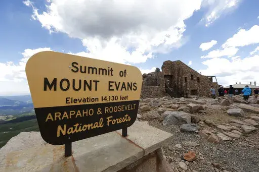 FILE— Visitors pass the sign on the summit of Mount Evans near Idaho Springs, Colo., on July 15, 2016. A Colorado state panel recommended Thursday, Nov. 17, 2022, that Mount Evans, a prominent peak near Denver, be renamed Mount Blue Sky.  (AP Photo/David Zalubowski, File)