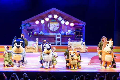 This image shows characters, from left, Bandit, Bluey,  Bingo and Chili and their puppeteers during a performance of “Bluey’s Big Play." The theatrical adaptation of the popular animated children’s TV show “Bluey” starts a multistate tour this month. (Darren Thomas via AP)