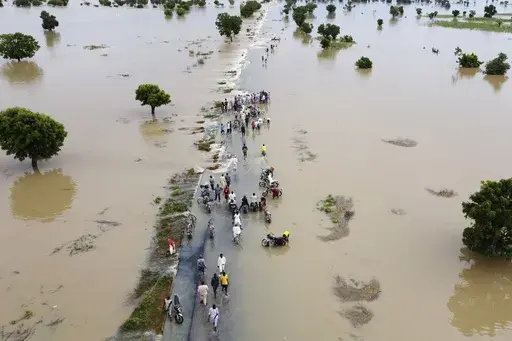 People walk through floodwaters after heavy rainfall in Hadeja, Nigeria, Sept 19, 2022. Publication of a major new United Nations report on climate change is being held up by a battle between rich and developing countries over emissions targets and financial aid to vulnerable nations. (AP Photo, File)