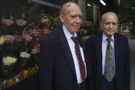 Octogenarian brothers from Ecuador, Carlos Cevallos, left, and Miguel Cevallos, together during a press meeting, Monday Aug. 29, 2022, in New York. For years the Cevallos brothers made a living drawing posters for nightclubs, taco trucks and restaurants, attracting clients by word of mouth, but an Instagram account changed a lot of that. (AP Photo/Bebeto Matthews)