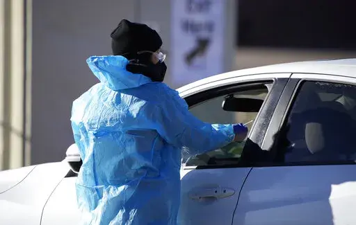A medical technician performs a nasal swab test on a motorist queued up in a line at a COVID-19 testing site near All City Stadium Dec. 30, 2021, in southeast Denver. Millions of workers whose jobs don’t provide paid sick days are having to choose between their health and their paycheck as the omicron variant of COVID-19 rages across the nation. While many companies instituted more robust sick leave policies at the beginning of the pandemic, those have since been scaled back with the rollout o