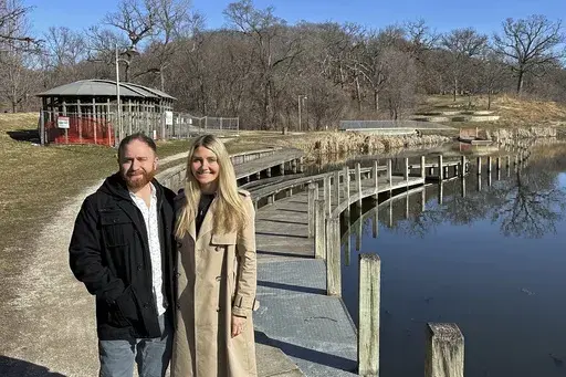 David and Stephanie Joiner pose by part of an artwork, called Greenwood Pond: Double Site, Sunday, Feb. 25, 2024, in Des Moines, Iowa. The Des Moines Arts Center plans to rip out the roughly 30-year-old artwork that lines a pond in a historic city park. The Joiners, who live about a mile from the pond, have been helping to organize local opposition to the artwork’s removal, including launching a website and simply engaging with people at the site to explain why parts are roped off. (AP Photo/S