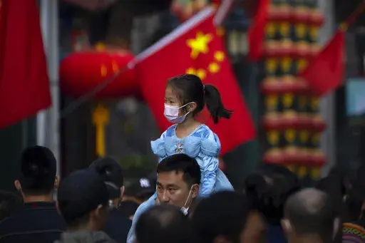 A girl wearing a face mask rides on a man's shoulders as they walk along a tourist shopping street in Beijing on Oct. 7, 2022. China has announced its first overall population decline in recent years amid an aging society and plunging birthrate. (AP Photo/Mark Schiefelbein, File)